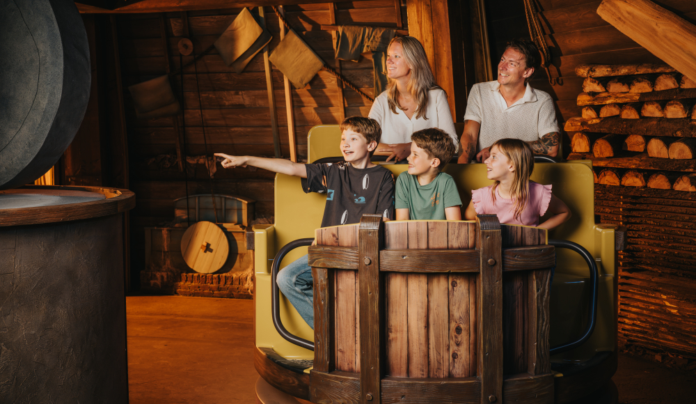 Gezin zit in een interactieve attractie in houtdecor; kind wijst enthousiast naar object links in beeld Gezin zit in een interactieve attractie in houtdecor; kind wijst enthousiast naar object links in beeld