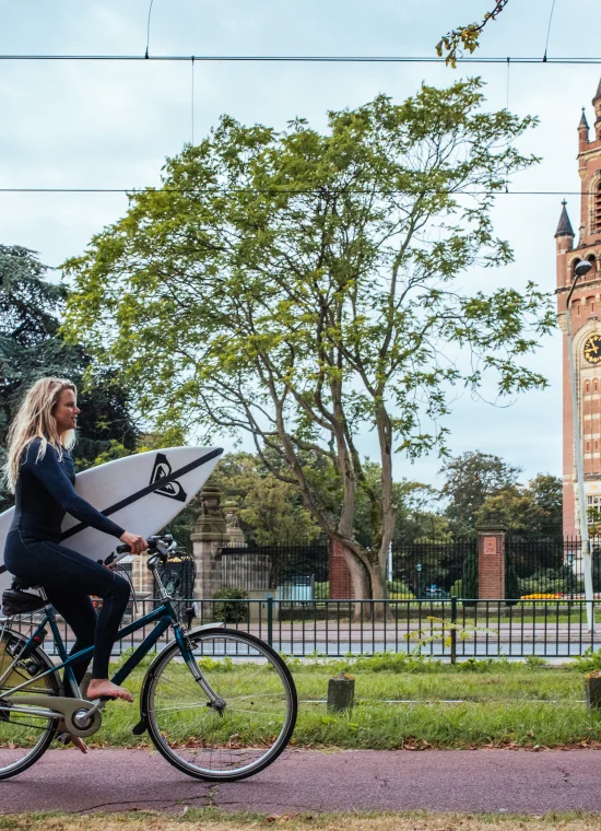 Zomer in Den Haag. Meisje met surfplank onder haar arm fiets langs het Vredespaleis richting Scheveningen