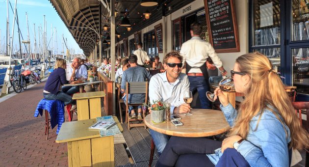 Zicht op restaurants en en mensen die een drankje drinken op terrassen langs de haven van Scheveningen op een zonnige dag