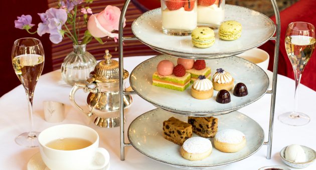 Luxe high tea met etagère vol zoetigheden, thee, champagne en bloemen op een elegant gedekte tafel