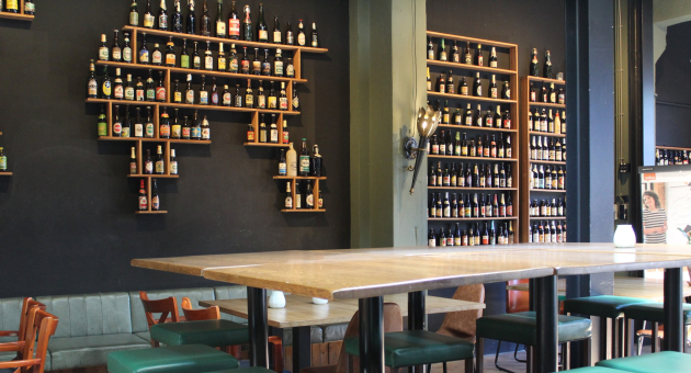 Biertafels bij Brouwerij De Prael met aan de muur een rek met verschillende biertjes.