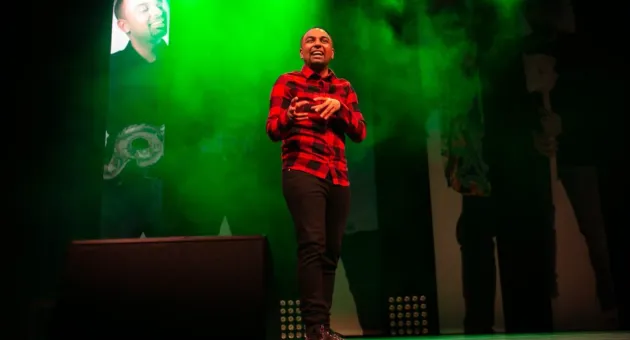 Man op toneel met groen licht en rode ruitjesbloes.