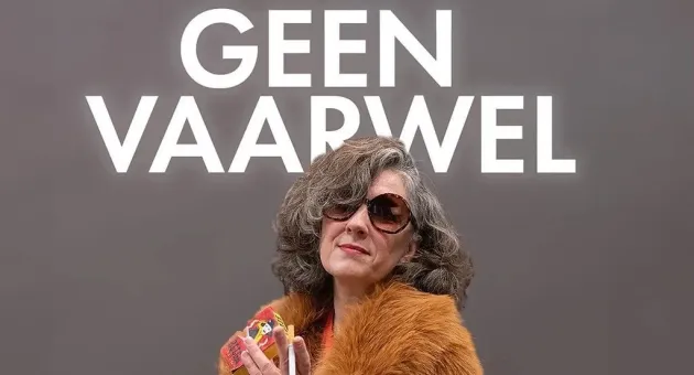 Naomi Inez Wielinga poseert voor een grijze achtergrond met de titel van haar show: Geen Vaarwel. Ze draagt een bruine bontjas en zonnebril. 