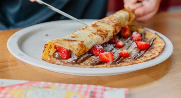 Pannenkoek met nutella en aardbeien en poedersuiker opgerolt.