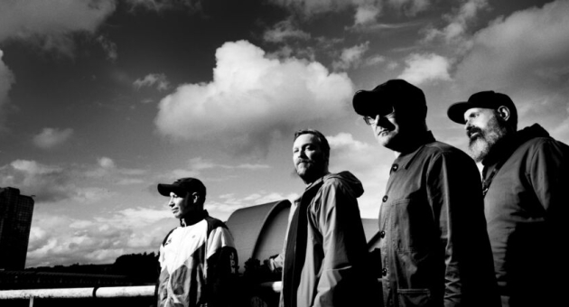 Bandfoto Mogwai in zwart/wit met wolken achtergrond.