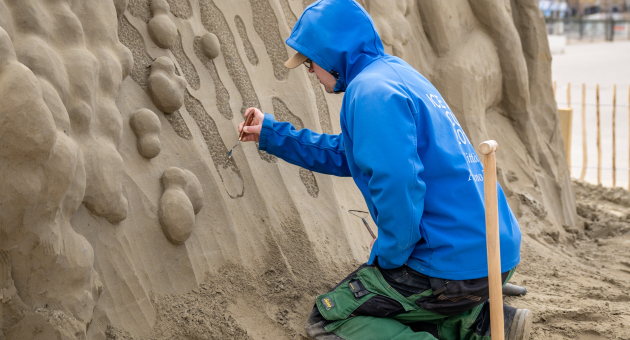 Zandsculptuur van golf met carver in blauwe jas