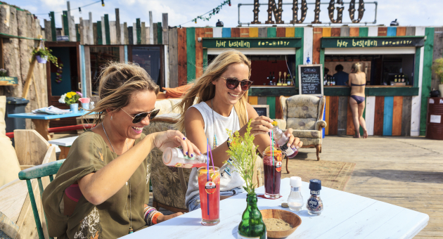 Twee dames genieten van een drankje op het strand bij Beachclub Indigo