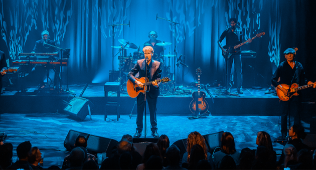Zanger Frank Boeijen op het podium met gitaar in blauw licht.