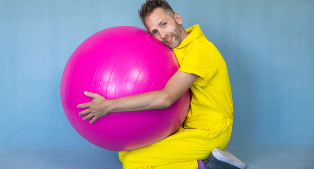 Promotiebeeld voor Peutervoorstelling Rokkerol Efrem Stein zit op de grond in een gele overal en knuffelt een grote roze bal 