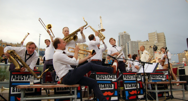 Moustache Big Band op bankjes Scheveningen spelend op instrumenten.