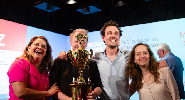 Winnaars poseren trots met grote gouden beker tijdens een prijsuitreiking van de Prinsjesfestival Pubquiz in Den Haag