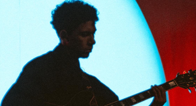 Portret van gitarist en producer Rafael Devánte Sinay in schaduw met een gitaar wat bpast bij de eerbetoon van de Nationale herdenking op 15 augustus.