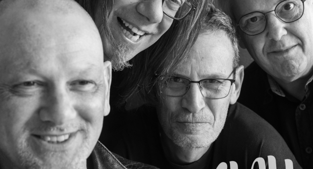 Zwart wit bandfoto van Slau enthousiast en lachend ingezoomd in de camera.