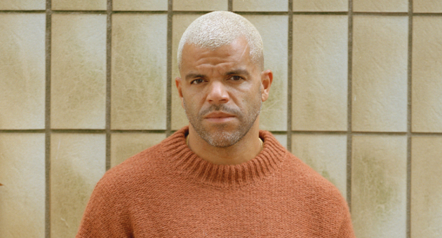 Zanger Sef serieus kijkend met een tegel achtergrond.