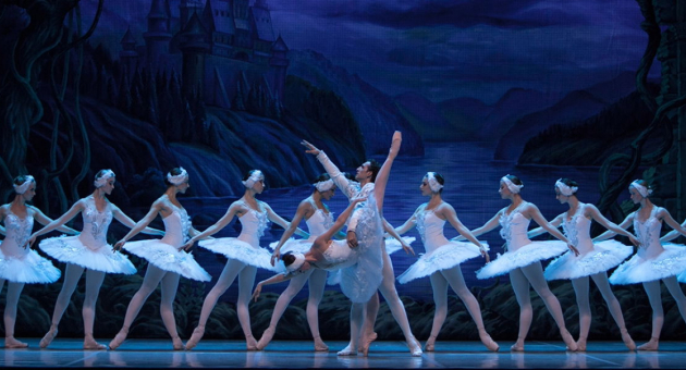 Balletdansers staan in hun witte tutu's en kostuums op het podium tijdens de productie van het zwanenmeer. 