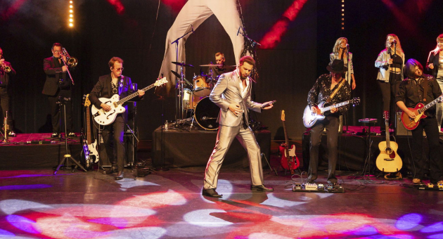 Bouke staat met de ElvisMatters Band op een rood verlicht podium in een gouden pak. 