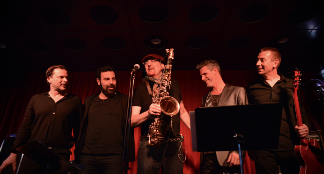 Bandfoto met de bandleden in donkere achtergrond met rood doek en een spot op hun gericht passend bij hun Bowie interpretatie.