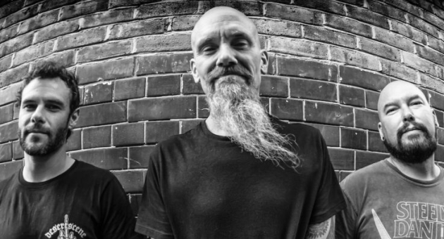 Zwart wit portret van Hardrock band Mondo Generator poserend tegen bakstenen muur.