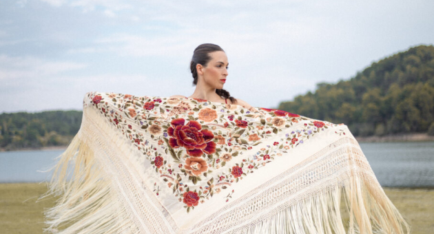 Foto in een Mediterrane omgeving met een meer en berg op de achtergrond waarin flamencodanseres Marina Paje met een mooie omslagdoek met opengestrekte armen staat.