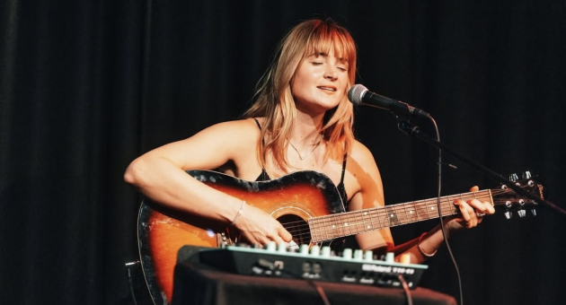 Een vrouwelijke artiest spelend op haar gitaar op het podium