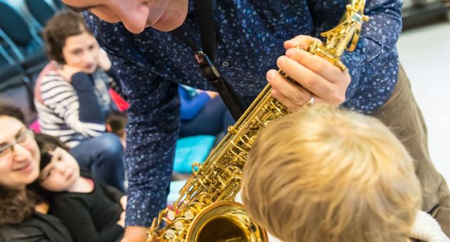 Een peuter kijkt naar de saxofoon van een muzikant tijdens het Ukkieconcert in Theater de Regentes