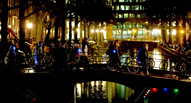 Wandelaars met lichtjes steken ’s avonds een brug over in een verlichte stad