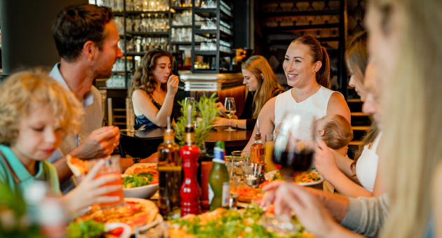 Gezellige familiescène in een restaurant waar mensen genieten van verse pizza en elkaars gezelschap. Een warme, ontspannen sfeer met lachende gezichten.