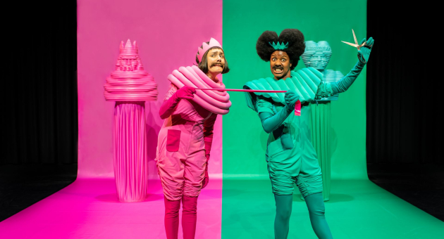 Twee acteurs in felroze en felgroen kostuum op gesplitst podium, met decor in bijpassende kleuren