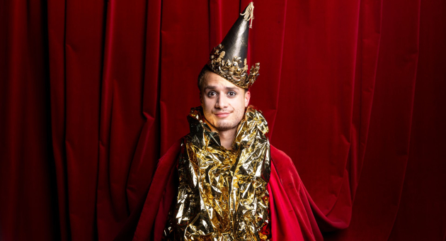 Persoon in feestelijke outfit met gouden folie en puntige kroon, voor rood fluwelen gordijn