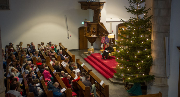 Een volle kerk tijdens een kerstbijeenkomst met een kerstboom.
