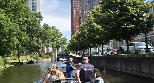 Een boot van de Ooievaart, vaart door de Haagse grachten met op de achtergrond de moderne skyline van Den Haag