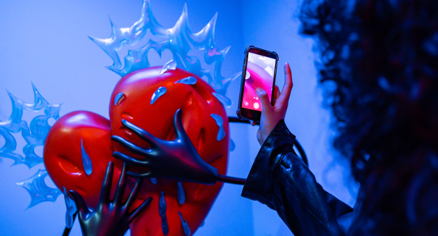 Rood hartsculptuur met handen en een smartphone.