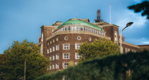 Een historisch gebouw met een groene koepel en bomen op de voorgrond.
