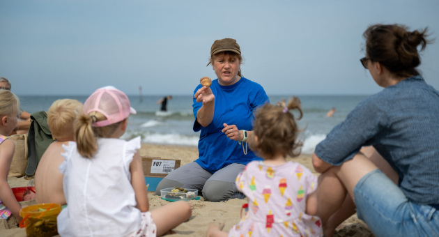 Een vrouw vertelt kinderen iets op het strand.