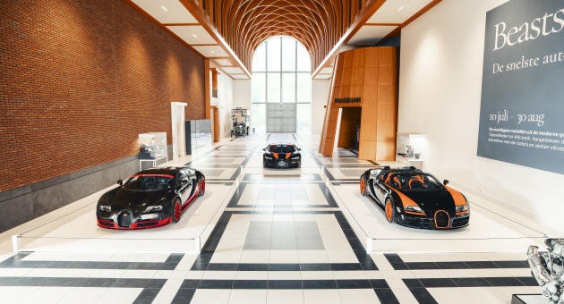 Three Bugatti sports cars are displayed in a museum hall.