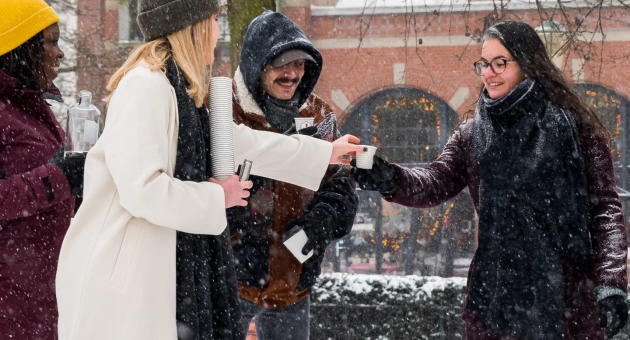 Groep mensen in de sneeuw, uitwisselend warme dranken.