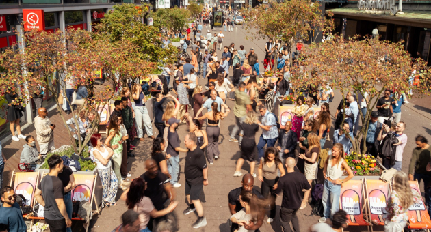 Mensen dansen en genieten op straat met bomen en bloemen. (c) Eric Hornman