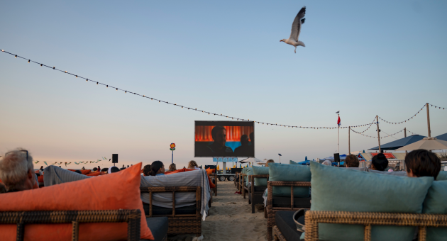 Mensen kijken naar een film op een groot scherm op het strand