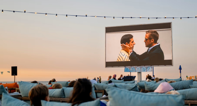 Mensen kijken naar een film op een groot scherm bij zonsondergang.