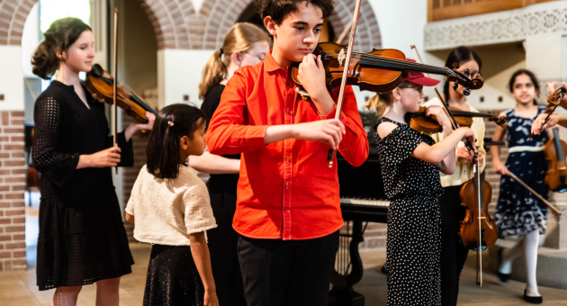 Leerlingen van Jong KC Muziek staan door elkaar en spelen viool. 