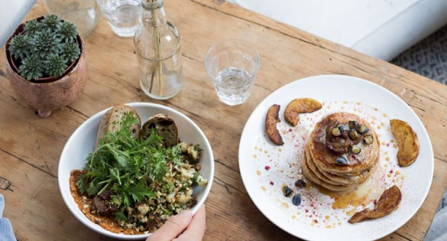 Een tafel in restaurant Plenty met een plantje en droogbloemen waarop een kom sla een boord pancakes staat.