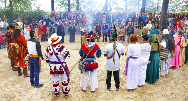 Groep mensen in traditionele kledij tijdens een ceremonie in een bos.