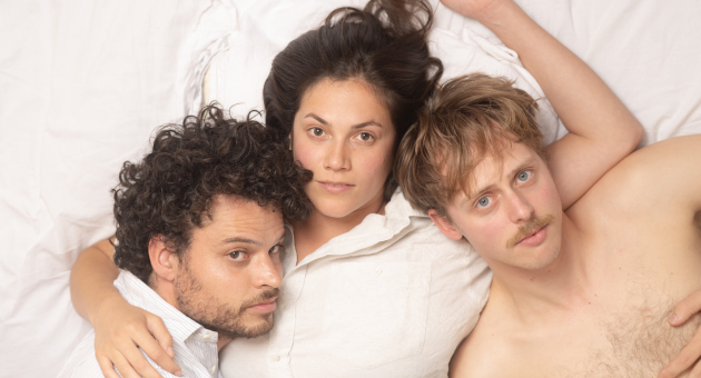 Drie personages liggen op een bed, met gezichten naar de camera. foto: Niels Knelis