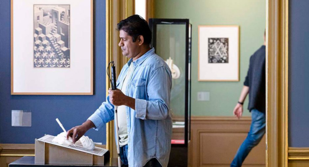 Man met blindegeleidestok voelt aan een werk van Escher tijdens een tour voor blinden en slechtzienden