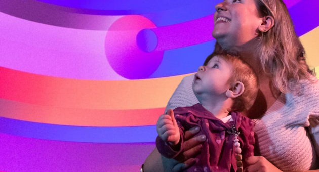 Baby-symfonie. Een moeder houdt een baby vast terwijl ze omhoog kijkt naar kleurrijke patronen op de muur.