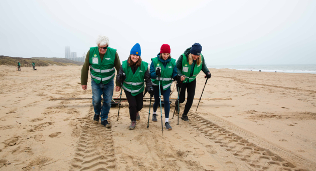 Vrijwilligers met groene vesten wandelen op het strand. (c) Eveline van Egdom