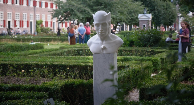 Witte buste in een groene tuin met mensen op de achtergrond.