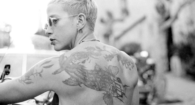 Portret van een persoon met korte haren en een tatoeage op de rug.