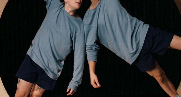 Twee acrobaten hangen in een houten cirkel en kijken naar elkaar.