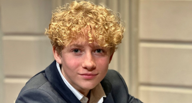 Een jongen met blond, krullend haar en een grijze blazer.